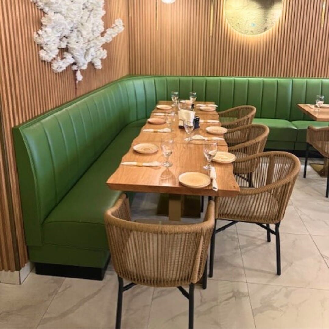 Custom green vinyl booth with rustic red-oak plank table on gold dual-post base and rope armchairs—space-efficient café seating.